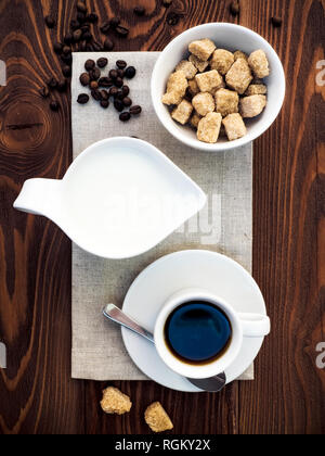 Tasse Kaffee, Milchkännchen, Schüssel mit Zucker und Kaffee Bohnen auf dem grau Serviette auf den Holztisch. Ansicht von oben Stockfoto