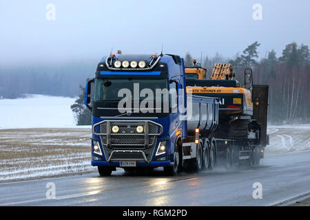 Salo, Finnland - 4. Januar 2019: Blaue Volvo FH Truck von M. Toivonen Oy hols Raupenbagger am Anhänger entlang nasse Autobahn an einem nebligen Tag im Winter. Stockfoto