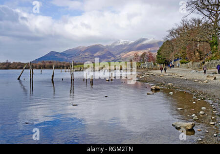 Touristen entlang Derwentwater See durch hölzerne Stege, kalten Wintertag, schneebedeckte Skiddaw hinter steigen, Lake District, Cumbria England Stockfoto