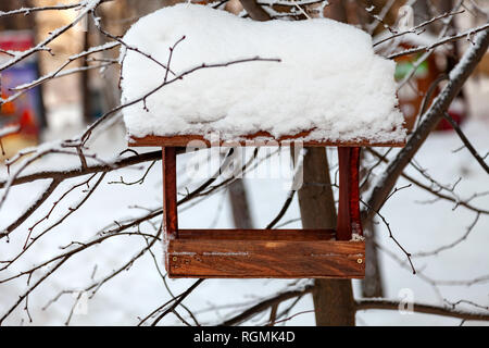 Nahaufnahme einer Holz- Vogelhaus Futterhaus mit einer großen Schicht von Schnee An einem klaren Wintertag in einem Wald von einem Baum aufgehängt abgedeckt Stockfoto