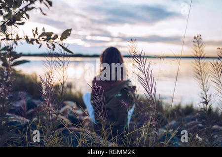 Junge Frau sitzt am See Inari, in Aussicht suchen, Finnland Stockfoto
