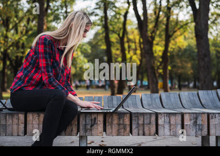 Junge Frau sitzt auf der Bank im freien Arbeiten am Laptop Stockfoto