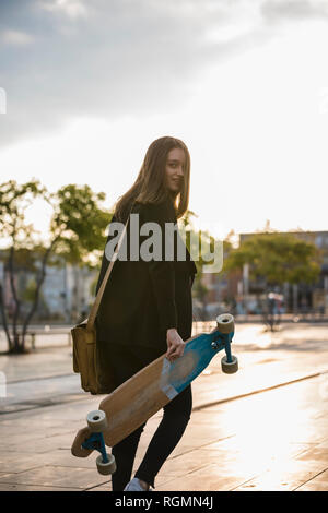 Junge Frau mit dem Longboard in der Stadt in Bewegung Stockfoto