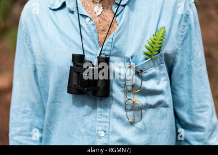 Junger Mann mit Fernglas und einem fer Blatt in seiner Hemdtasche Stockfoto