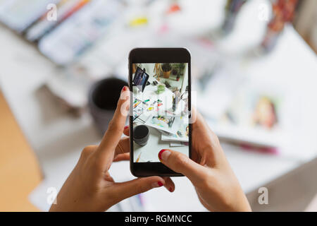Der Illustrator Hände unter Foto von Schreibtisch im Atelier mit Smartphone, close-up Stockfoto