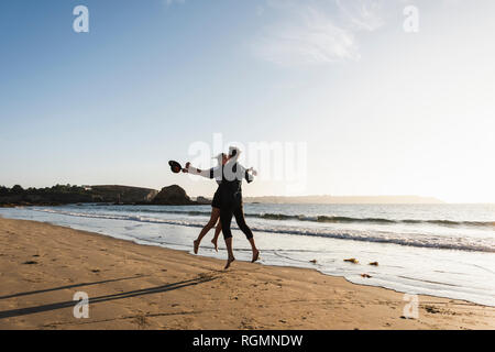 Frankreich, Bretagne, glückliches junges Paar am Strand bei Sonnenuntergang springen Stockfoto