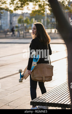 Junge Frau mit dem Longboard in der Stadt in Bewegung