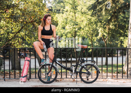 Passen junge Frau mit Fahrrad, lehnte sich auf Geländer in einem Park Stockfoto