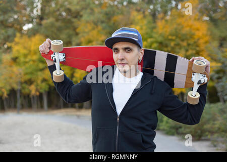 Porträt der Mann mit dem Skateboard auf den Schultern im Herbst Stockfoto