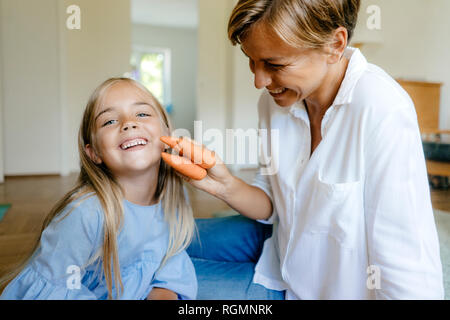 Glückliche Mutter und Tochter mit Karotten zu Hause Stockfoto