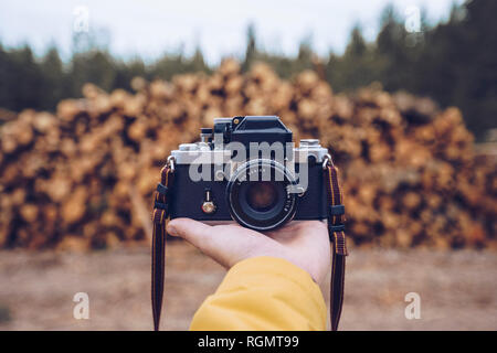 Hand, die eine Kamera vor einem Stapel Holz Stockfoto