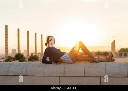Spanien, Barcelona, Montjuic, junge Frau an einer Wand bei Sonnenuntergang liegen Stockfoto