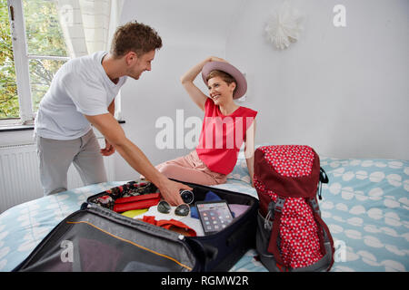 Glückliches Paar packen Koffer für Sommerferien auf Bett Stockfoto