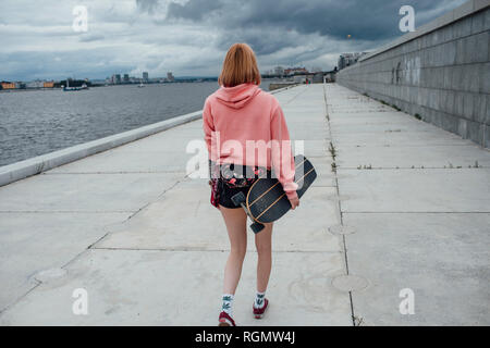 Ansicht der Rückseite des junge Frau mit Carver skateboard Wandern am Flußufer Stockfoto