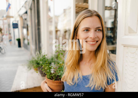 Niederlande, Maastricht, lächelnde blonde junge Frau mit Blumentopf in der Stadt Stockfoto