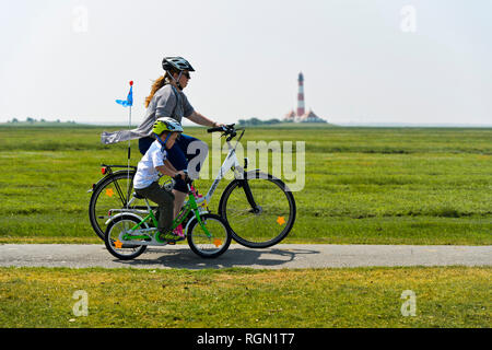 Mutter und Kind auf einem Fahrrad Exkursion in den Nationalpark Schleswig-Holsteinisches Wattenmeer, Leuchtturm Westerheversand hinter, Westerhever, Deutschland Stockfoto