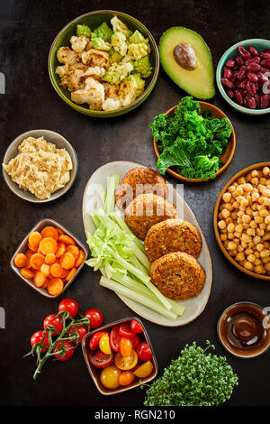 Bunte levante Küche Essen auf Gerichte voller rohes Gemüse und vorbereiteten Koteletts Overhead auf dunklem Hintergrund gesehen serviert. Stockfoto