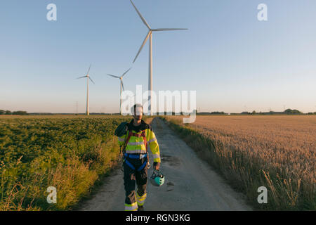 Techniker gehen auf Feld Pfad in einen Windpark mit Kletterausrüstung Stockfoto