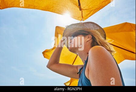 Lächelnde Frau mit Strohhut unter sunsahde im Sonnenlicht Stockfoto
