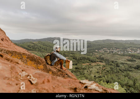 Junger Mann mit Rucksack, sitzen auf einem Berg, mit Blick auf Blick Stockfoto