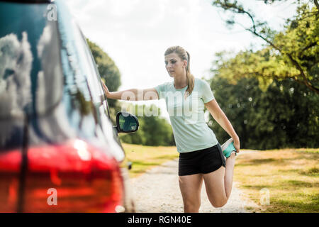 Sportliche junge Frau, die sich in einem Auto in einem Park Stockfoto