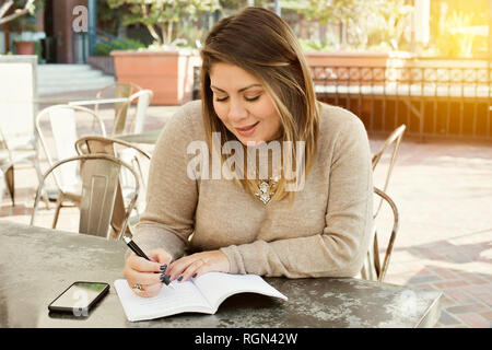 Junge Latina schreibt ihre Ziele in einem Journal draußen in einem Café Stockfoto