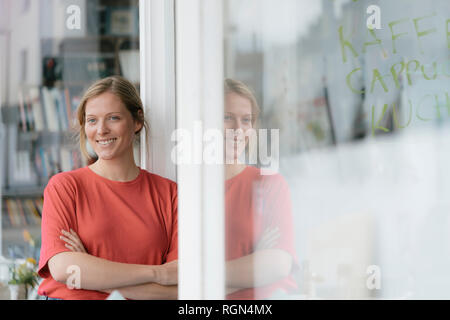 Portrait von lächelnden jungen Frau an der französische Tür in einem Cafe Stockfoto