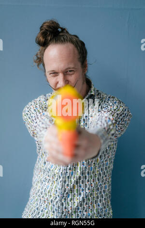 Porträt der Mann mit Schnurrbart holding Wasserpistole an der blauen Wand Stockfoto