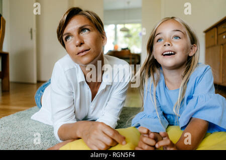 Mutter und Tochter auf dem Boden liegend zu Hause beobachten etwas Stockfoto