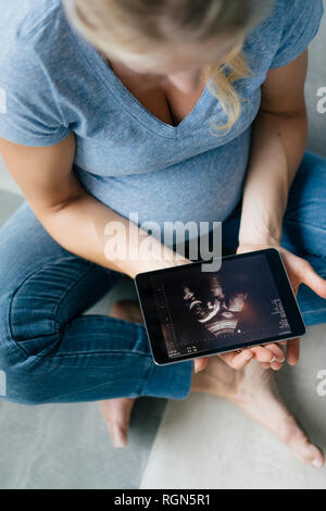 Schwangere Frau auf dem Boden sitzend mit Ultraschall Bild auf Tablet