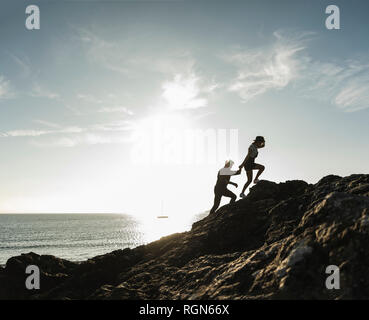 Frankreich, Bretagne, junges Paar klettern auf einem Felsen am Strand bei Sonnenuntergang Stockfoto