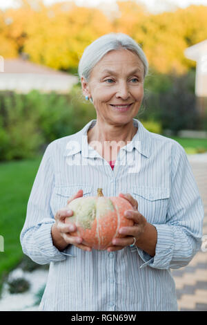 Portrait von lächelnden älteren Frau mit Geernteten Kürbis im Garten Stockfoto