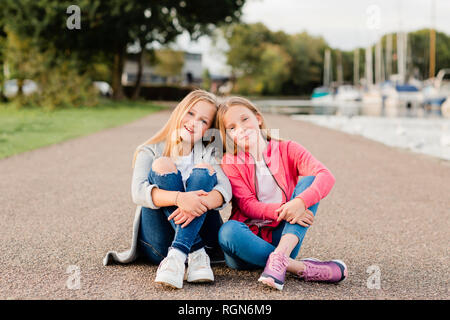 Portrait von zwei lächelnde Mädchen sitzen Kopf auf den Boden zu Kopf Stockfoto