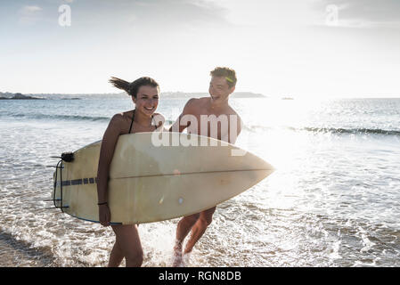 Frankreich, Bretagne, glückliches junges Paar mit Surfbrett im Meer läuft Stockfoto