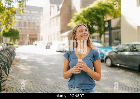 Niederlande, Maastricht, lächelnde blonde junge Frau mit Eis in der Stadt Stockfoto