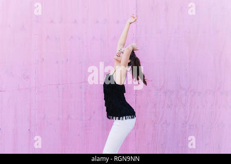 Glückliche junge Frau stand vor der rosa Wand Stockfoto