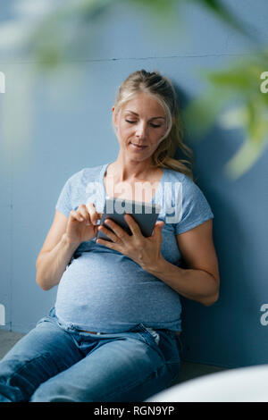 Schwangere Frau auf dem Boden sitzend mit Tablet Stockfoto