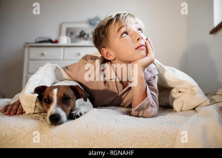 Porträt der blonde Junge und seine Jack Russel Terrier zusammen liegend auf Bett Stockfoto