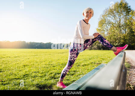 Lächelnde ältere Frau, die sich auf einer Bank in ländlichen Landschaft Stockfoto