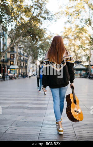Rothaarige Mädchen mit einer Gitarre in der Stadt, Ansicht von hinten Stockfoto