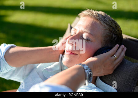 Portrait von Frau Musik hören mit Kopfhörern im Garten Stockfoto