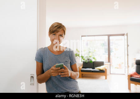 Porträt der lächelnde Frau zu Hause holding Handy Stockfoto