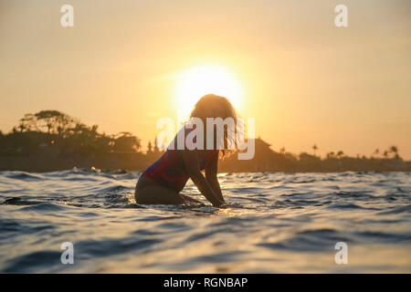 Indonesien, Bali, schwangere Frau sitzt auf Surfboard bei Sonnenuntergang Stockfoto