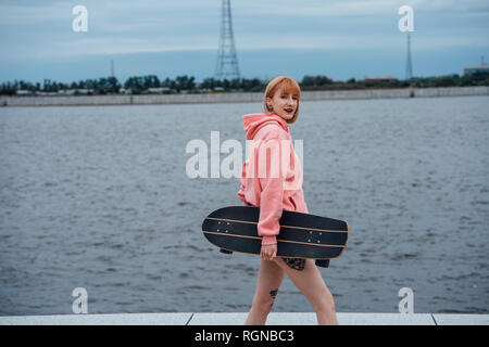 Junge Frau mit Carver skateboard Wandern am Flußufer Stockfoto