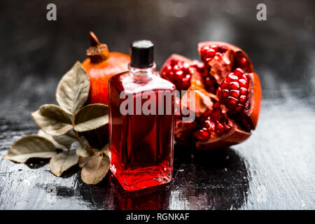 Nahaufnahme von ätherischen Öl der Granatapfel mit roh reif Granatapfel auf Holz- Oberfläche in transparente Flasche. Stockfoto