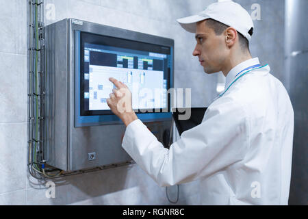 Techniker mit einem Laptop in der Hand in der Nähe der Monitor in der milchfabrik Stockfoto