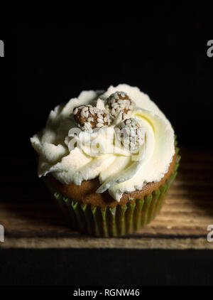 Beleuchtete Cupcakes auf einem Holzbrett auf schwarzem Hintergrund Stockfoto