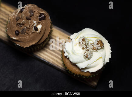 Beleuchtete Cupcakes auf einem Holzbrett auf schwarzem Hintergrund Stockfoto