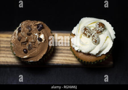 Beleuchtete Cupcakes auf einem Holzbrett auf schwarzem Hintergrund Stockfoto