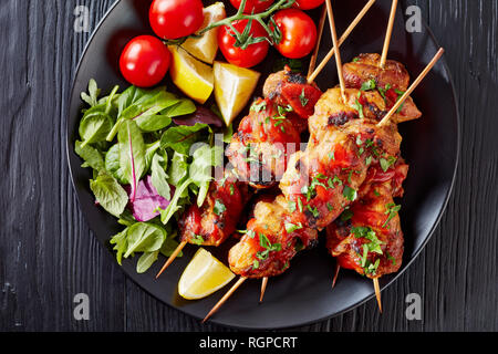 Ansicht von oben Der chicken Kebab gegrillt auf Spieße mit Salat, Zitrone Keile auf einer schwarzen Platte, auf einem Holztisch, Ansicht von oben, Kopie, c Stockfoto